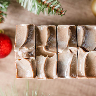 Top view of Noggy Holidays cold process soap bar topped with sparkles and surrounded by red ornaments and christmas tree decor