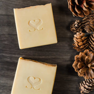 Two bars of Fireside Mountain Retreat cold process soap on a wooden background surrounded by pine cones