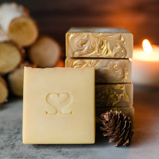 Fire in the background, close up of Fireside Mountain Retreat cold process soap bar on a cement surface with pine cones and wooden logs nearby