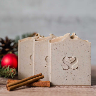 Three Noggy Holidays cold process soap bars with a cinnamon stick, red ornaments and christmas tree decor